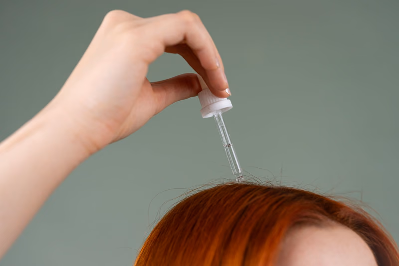 A dropper of treatment held above copper hair