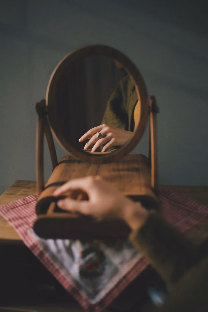 A hand resting on a wooden vanity beside a round mirror